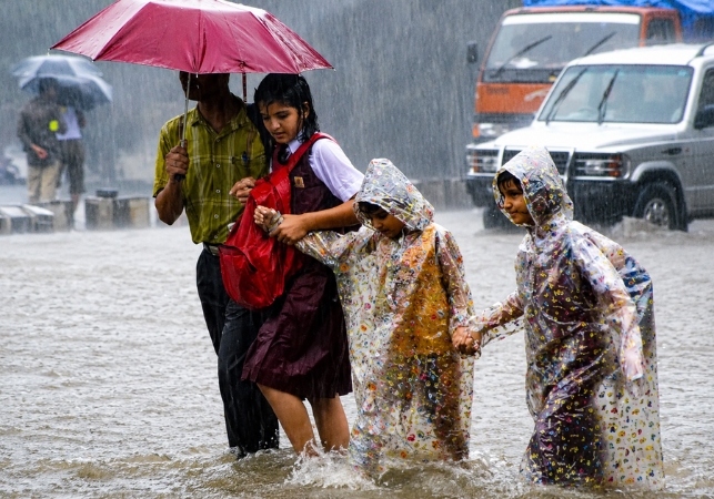 Children wading through flooded streets in heavy monsoon rain, highlighting the need for organisations like Spreading Bliss Foundation to support vulnerable communities.

