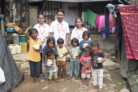 Spreading Bliss Foundation volunteers distribute food to children in an underserved community, with children holding meal containers.